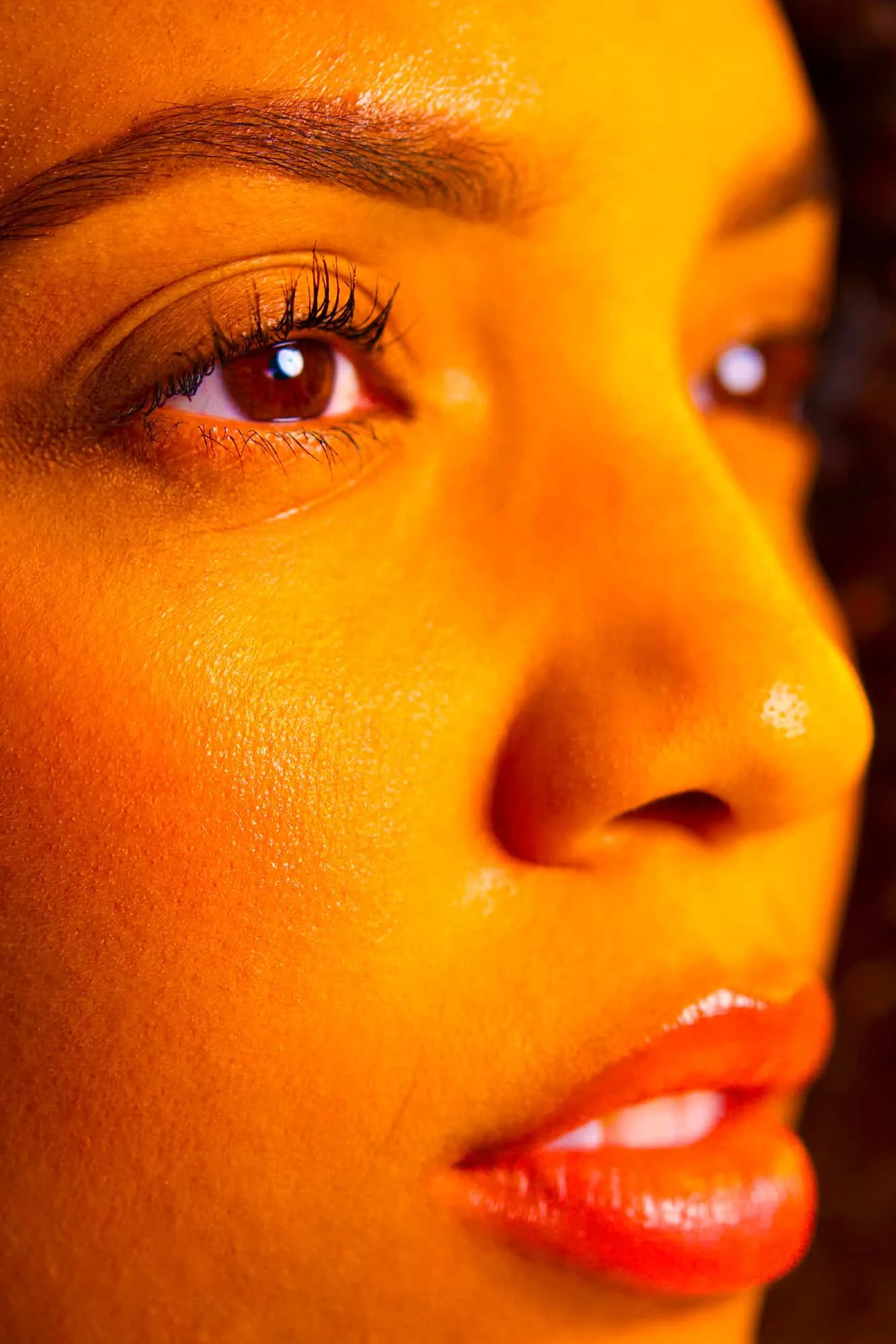 Side-profile close-up of a woman’s face with radiant golden skin and glossy lips