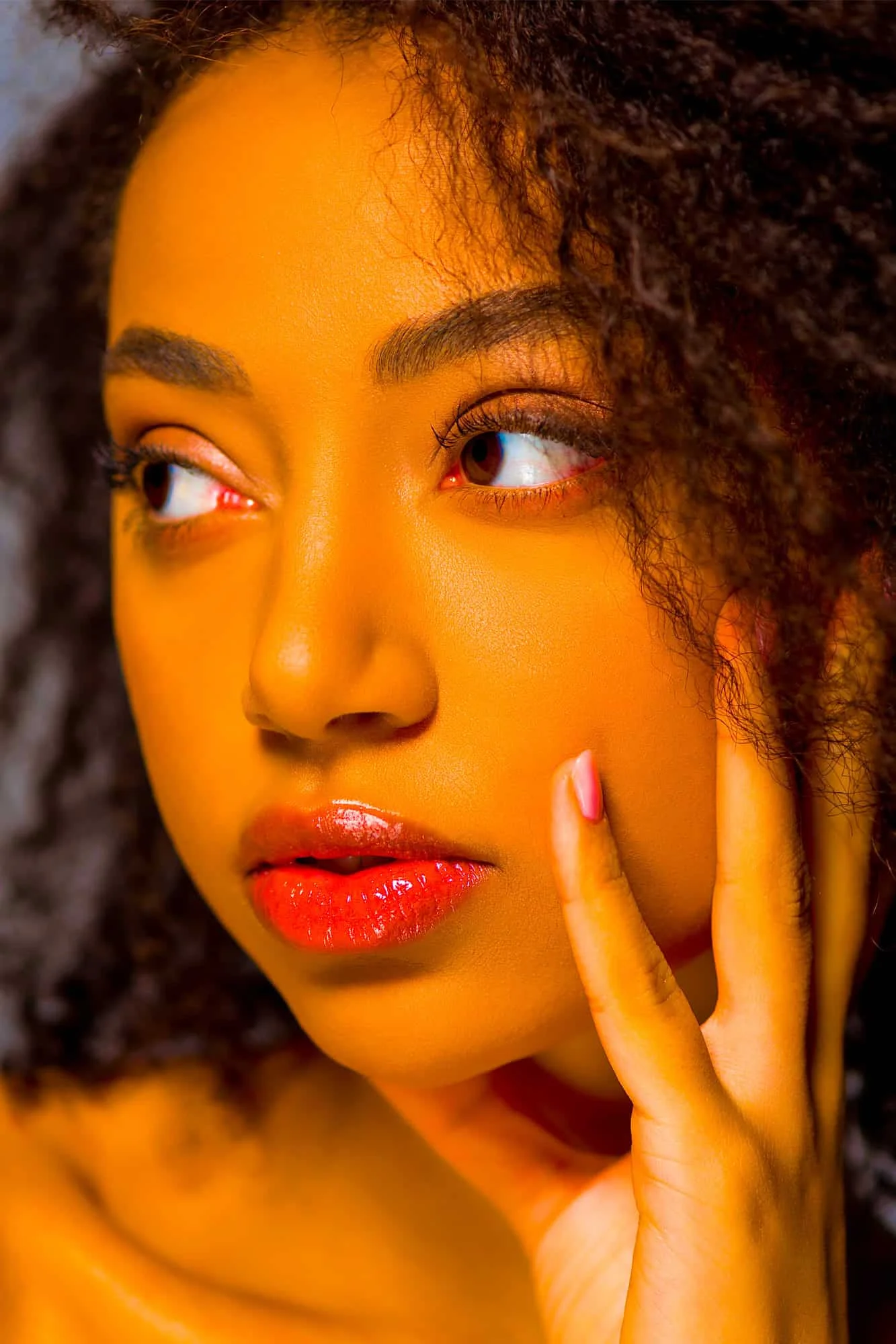 Close-up portrait of an elegant Black woman with curly hair in soft, warm light, gazing thoughtfully to the side